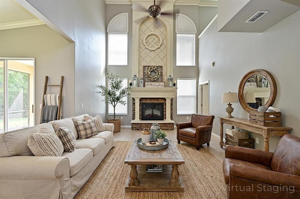 A living room features a tall fireplace, vaulted ceilings, neutral furniture, and a large area rug — 210 WINDING RIVER TRAIL, BRADENTON, FL