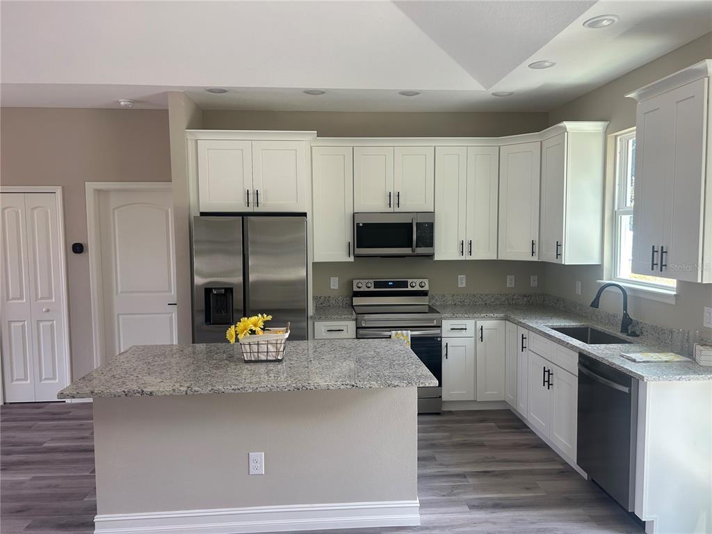 A kitchen features white cabinets, granite countertops, stainless steel appliances, and a central island — 1176 EIGHTH STREET, ORANGE CITY, FL