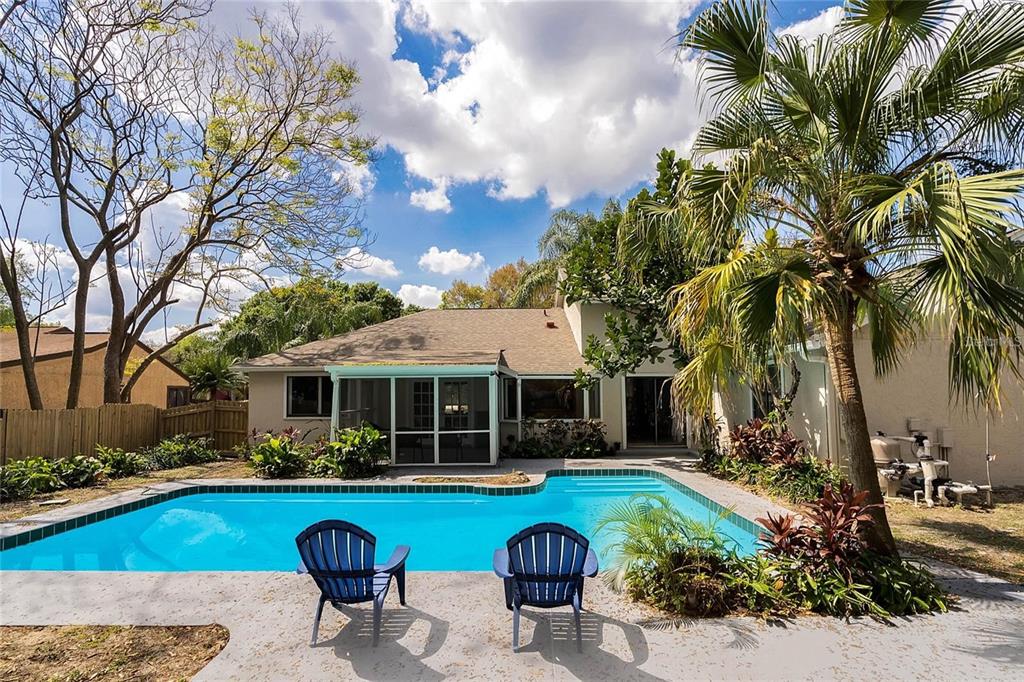 A backyard features a swimming pool, two blue chairs, a screened patio, and palm trees — 5607 SPRING RUN AVENUE, ORLANDO, FL