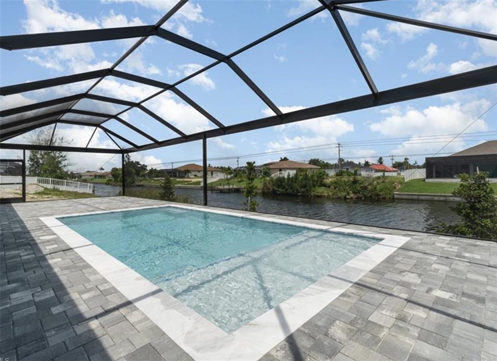 A rectangular swimming pool with a sun shelf sits inside a screened-in patio by a canal — 1801 SW 15TH PLACE, CAPE CORAL, FL