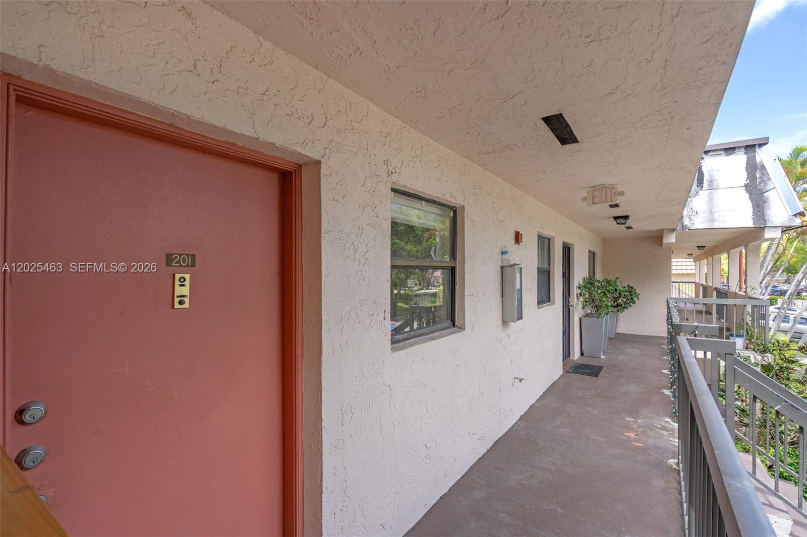 An exterior walkway leads to the entrance of unit 201 with a pink door — 841 NE 207th Ln # 201, Miami FL 33179, MIAMI, FL