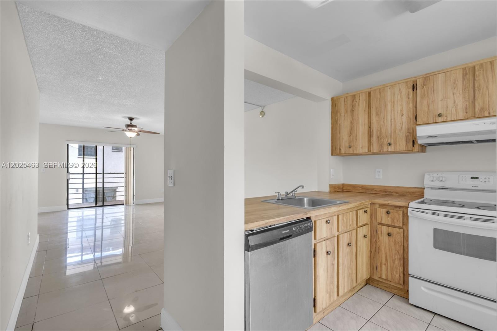 A kitchen with light wood cabinets and a stainless steel dishwasher overlooks a tiled living area — 841 NE 207th Ln # 201, Miami FL 33179, MIAMI, FL