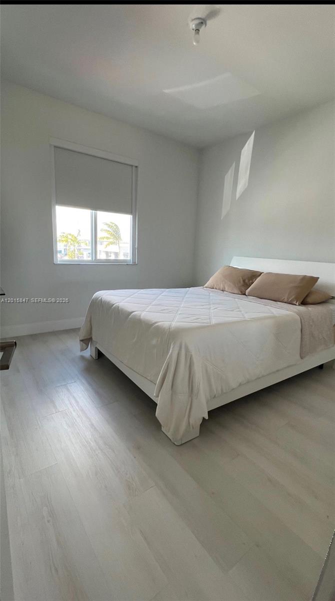 A bedroom features a white bed, light wood-look flooring, and a window with a shade — 686 SE 13th Ct, Homestead FL 33034, HOMESTEAD, FL