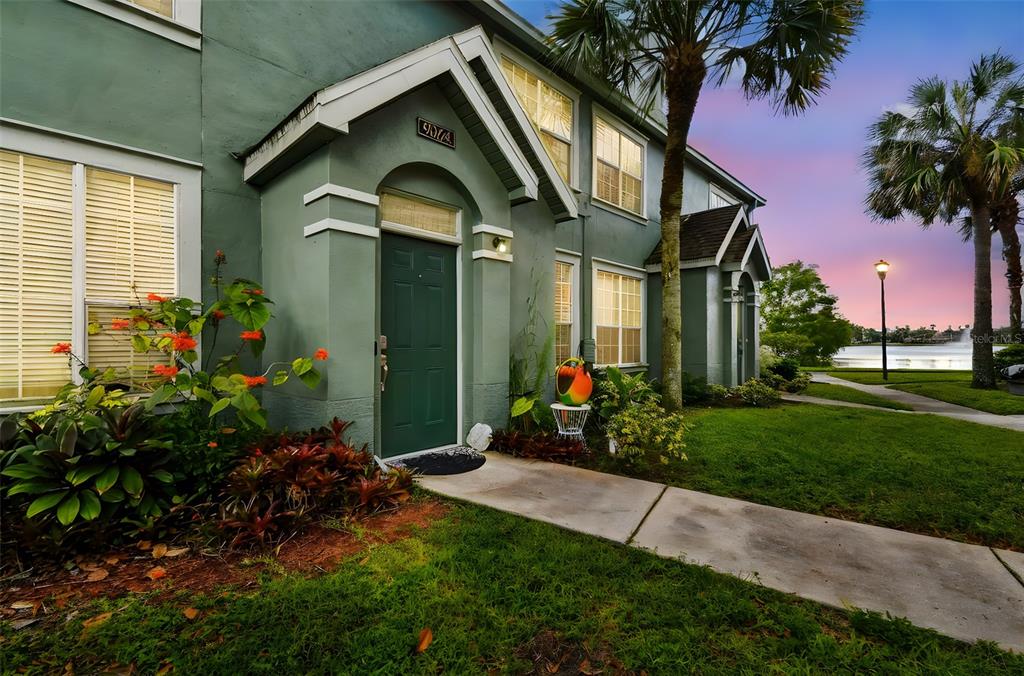 A green two-story townhouse exterior features a front entrance, landscaping, and a nearby lake — 9064 LAKE CHASE ISLAND WAY, TAMPA, FL