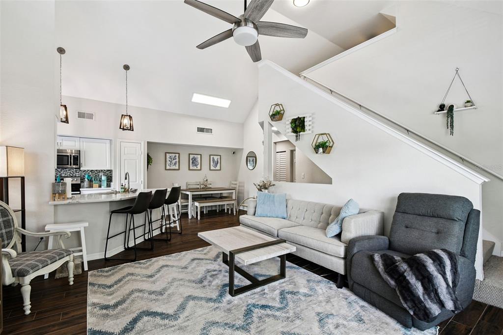 An open-concept living room and kitchen feature a vaulted ceiling, wood flooring, and neutral decor — 9064 LAKE CHASE ISLAND WAY, TAMPA, FL
