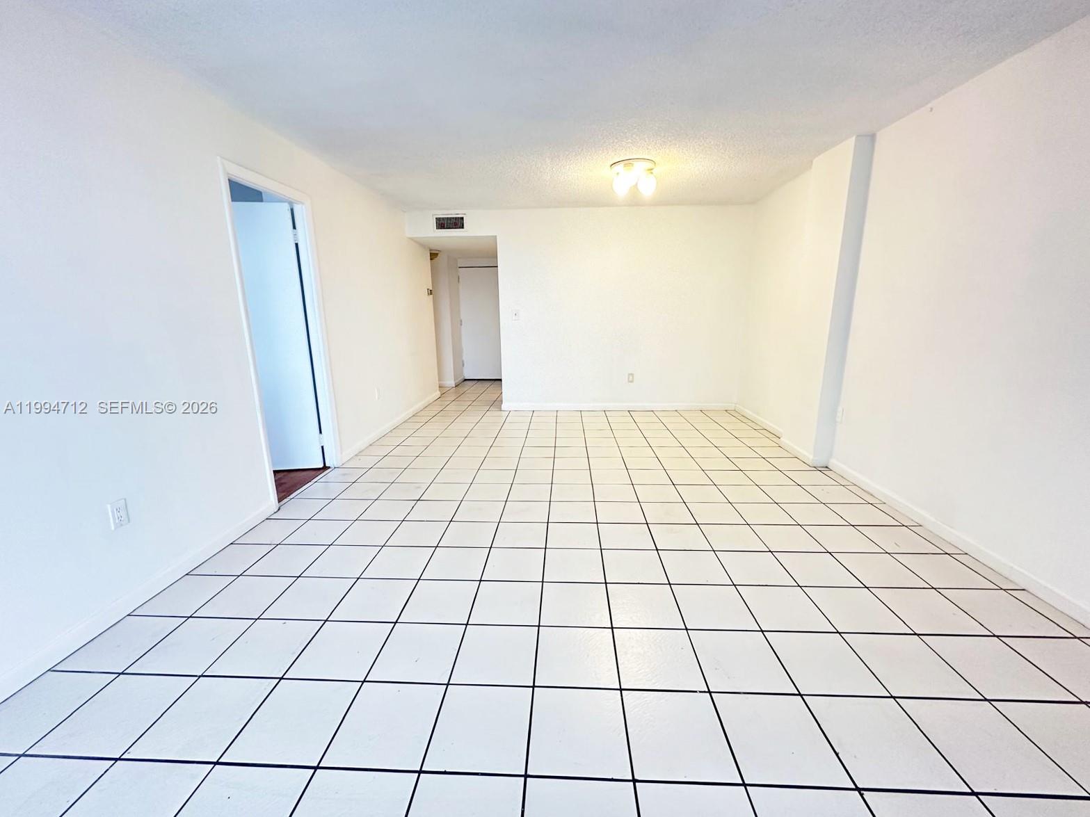 An empty room features white walls, a white tiled floor with dark grout, and a ceiling light — 15600 NW 7th Ave # 606, Miami FL 33169, MIAMI, FL