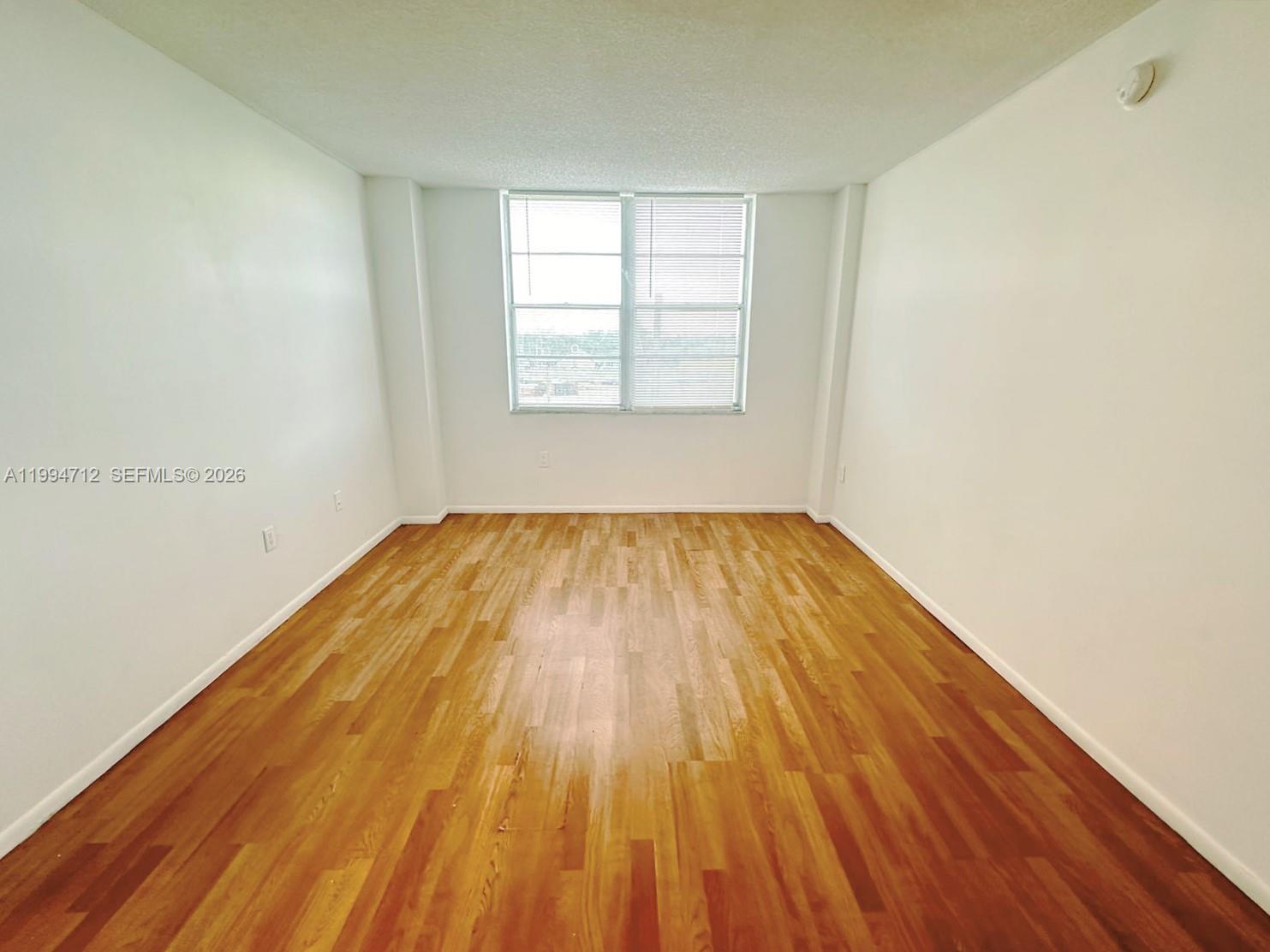 An empty room features white walls, light wood-look flooring, and a single window with blinds — 15600 NW 7th Ave # 606, Miami FL 33169, MIAMI, FL