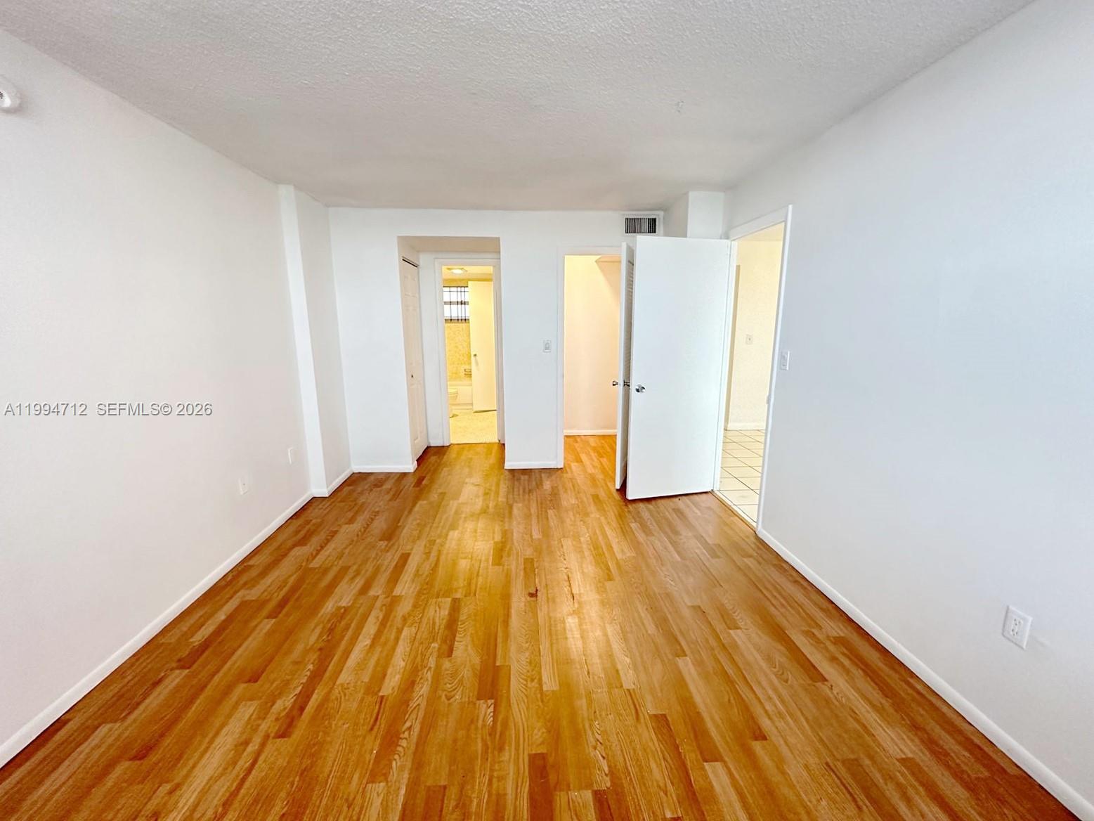 An empty room features white walls, light wood flooring, and two doorways leading to other areas — 15600 NW 7th Ave # 606, Miami FL 33169, MIAMI, FL