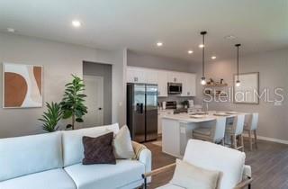 This open-concept kitchen and living area features white cabinetry, stainless steel appliances, and pendant lighting — 320 MARION OAKS COURSE, OCALA, FL