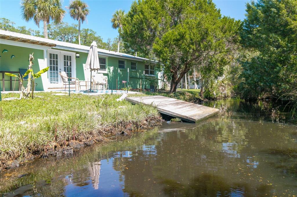 A green house with a patio and wooden dock sits beside a small canal — 10709 W HALLS RIVER ROAD, HOMOSASSA, FL