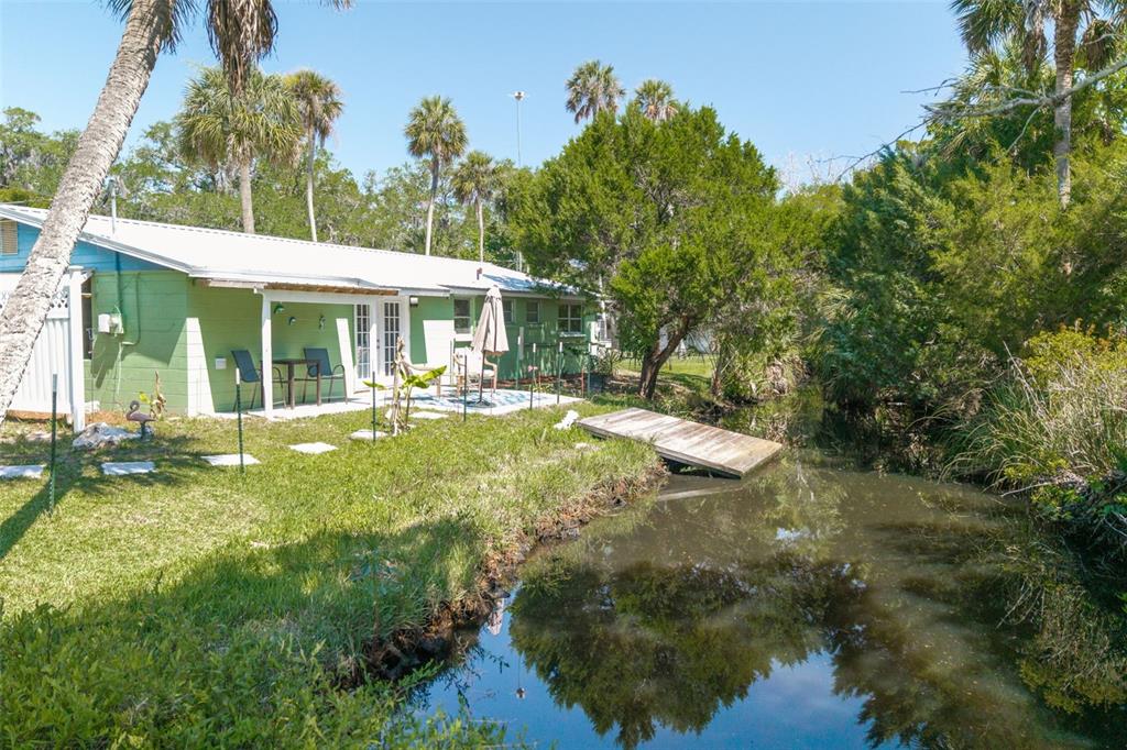 A green house with a white roof sits next to a small canal and dock — 10709 W HALLS RIVER ROAD, HOMOSASSA, FL