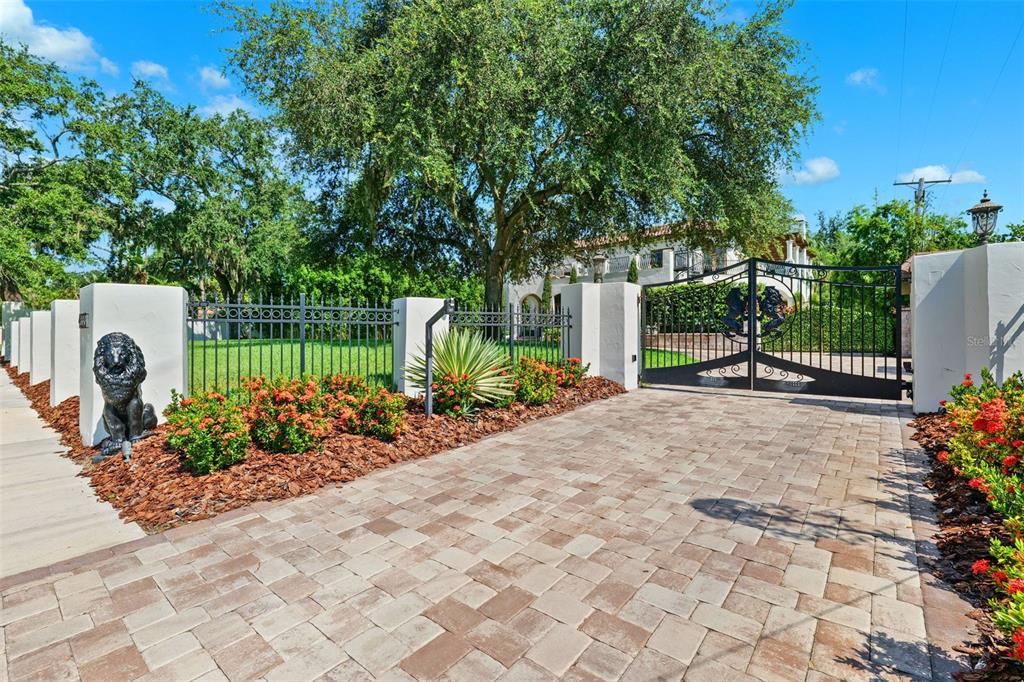 A paved driveway leads to a gated entrance with a lion statue and lush landscaping — 4555 W SWANN AVENUE, TAMPA, FL