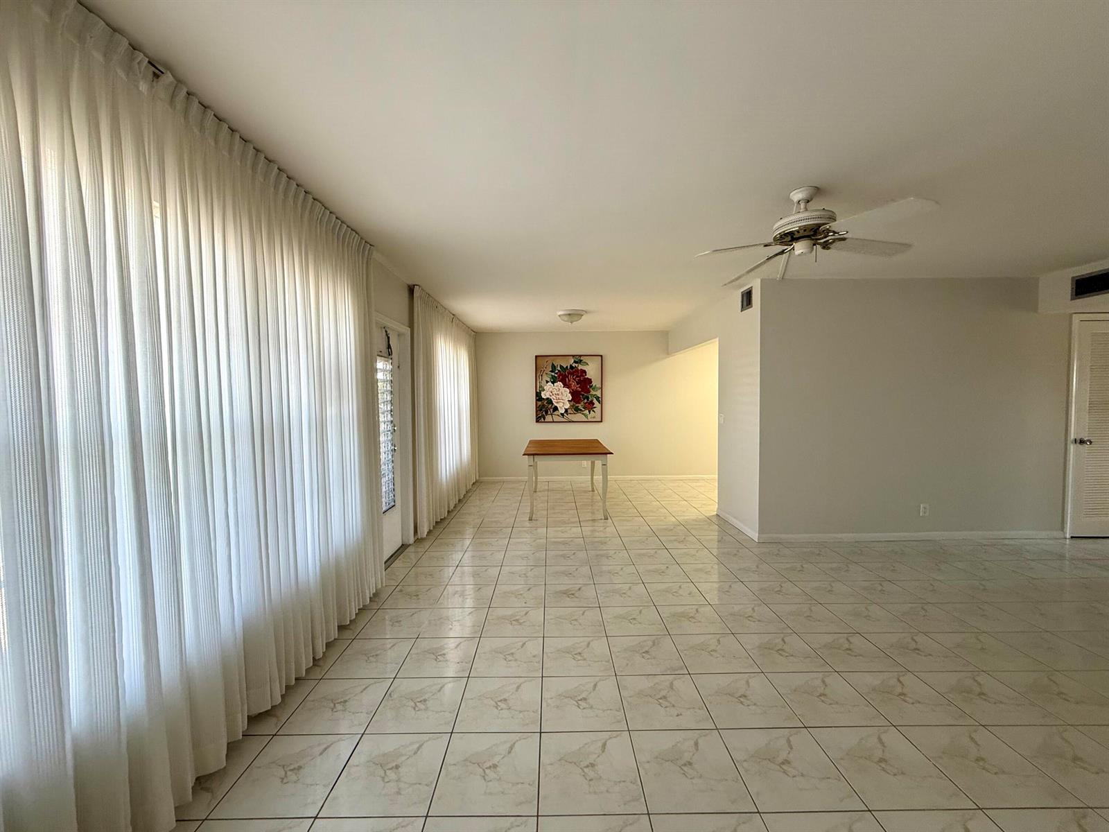 A spacious room with white tile flooring, floor-to-ceiling curtains, and a central dining table — 313 Greenbrier B, West Palm Beach FL 33417, WEST PALM BEACH, FL