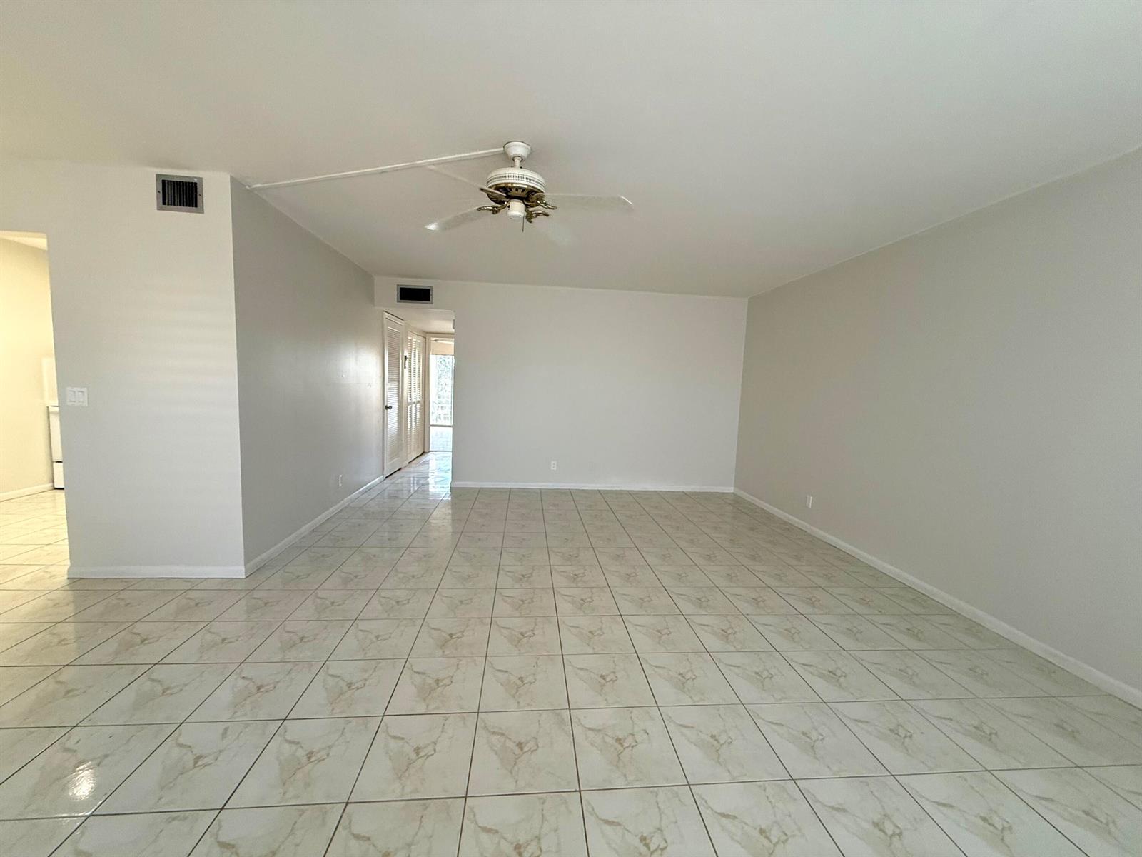 An empty living room features light-colored tile flooring, white walls, and a ceiling fan — 313 Greenbrier B, West Palm Beach FL 33417, WEST PALM BEACH, FL
