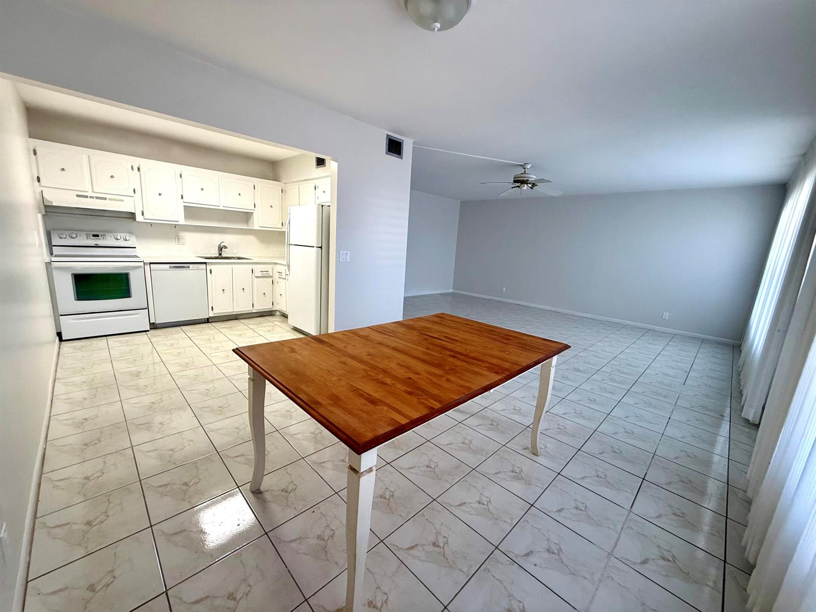 A kitchen with white cabinets and appliances opens to a large, tiled living area — 313 Greenbrier B, West Palm Beach FL 33417, WEST PALM BEACH, FL
