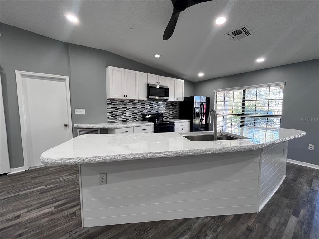 A kitchen features white cabinets, a stone-topped island, and a mosaic tile backsplash — 8122 MATTHEW DRIVE, NEW PORT RICHEY, FL