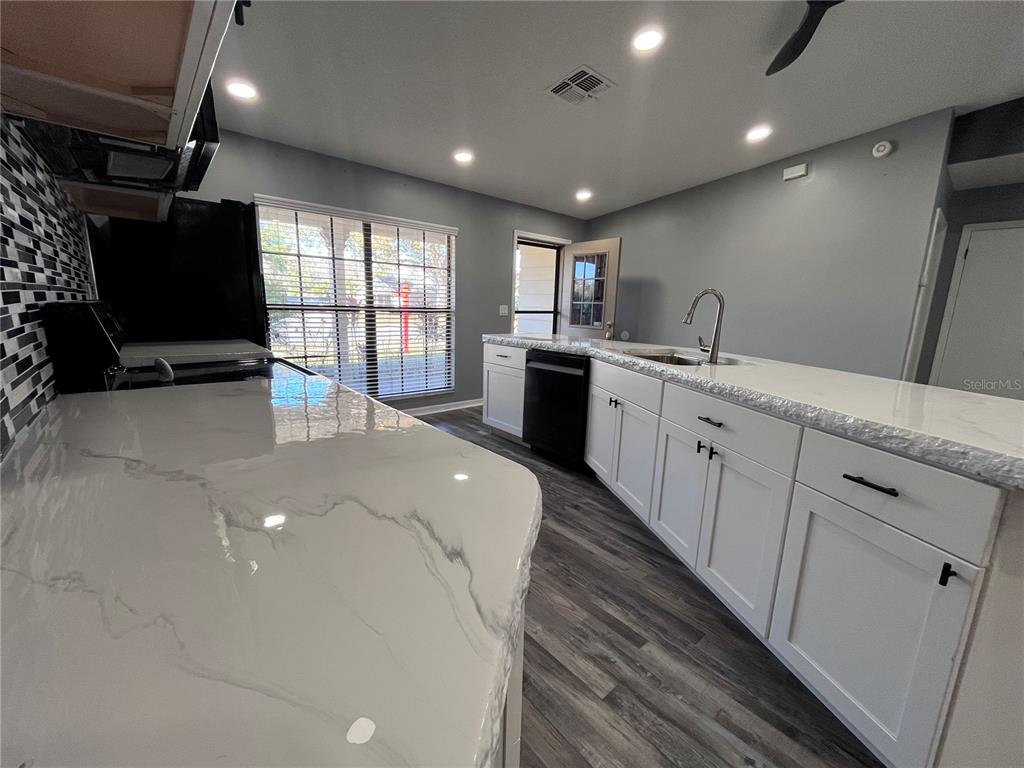 A kitchen features white cabinets, marble-look countertops, black appliances, and gray wood-look flooring — 8122 MATTHEW DRIVE, NEW PORT RICHEY, FL