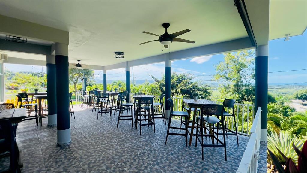 A covered outdoor patio features tiled flooring, multiple high-top tables, and scenic hillside views — Km 2.4 CARR 402, ANASCO, PR