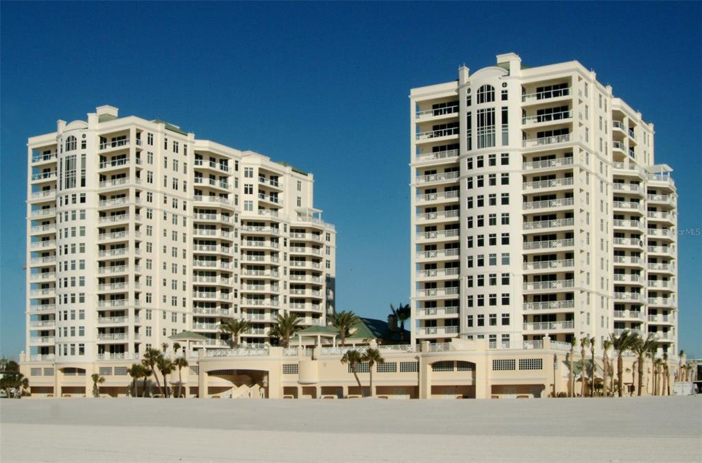 Two tall, white multi-story residential buildings stand side-by-side behind a wide, sandy beach — 10 PAPAYA STREET UNIT 1204, CLEARWATER, FL