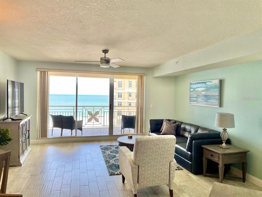 A living room features a black leather sofa, patterned armchair, and sliding doors overlooking the ocean — 10 PAPAYA STREET UNIT 1204, CLEARWATER, FL