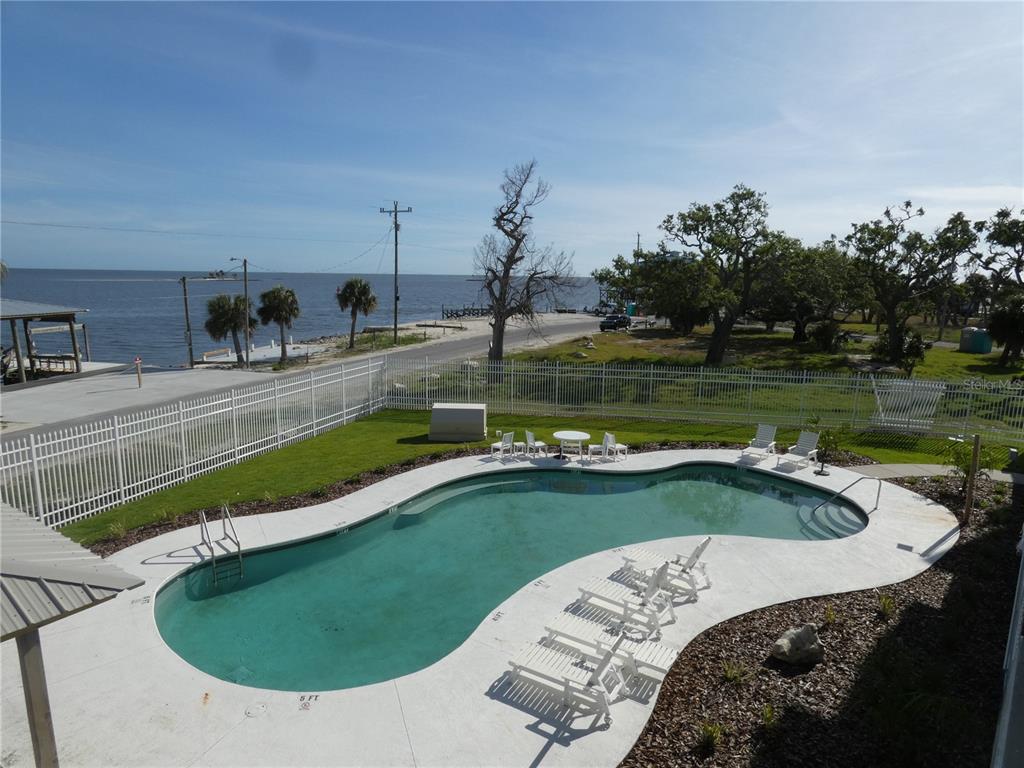 A kidney-shaped swimming pool sits in a fenced backyard overlooking a coastal waterfront view — 502 MAIN STREET UNIT 106, HORSESHOE BEACH, FL