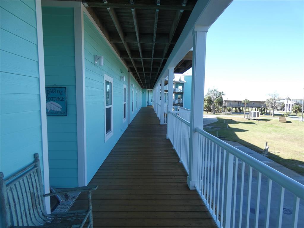 A long, covered wooden balcony with light blue siding and a white railing overlooks a yard — 502 MAIN STREET UNIT 106, HORSESHOE BEACH, FL