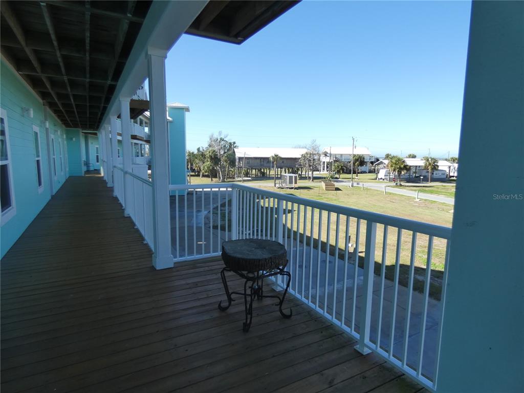 A wooden deck with a white railing overlooks a grassy area and nearby coastal buildings — 502 MAIN STREET UNIT 106, HORSESHOE BEACH, FL