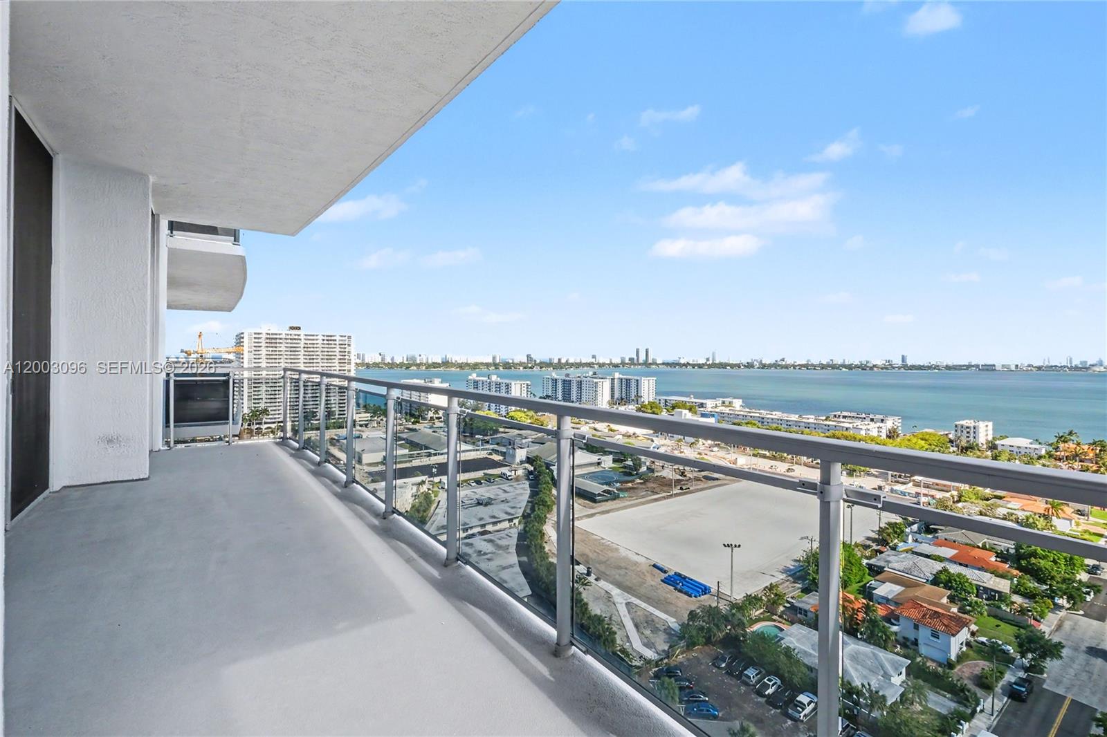 A high-rise balcony with a glass railing overlooks a bay and a city skyline — 7901 Hispanola Ave # 1810, Miami FL 33141, MIAMI, FL