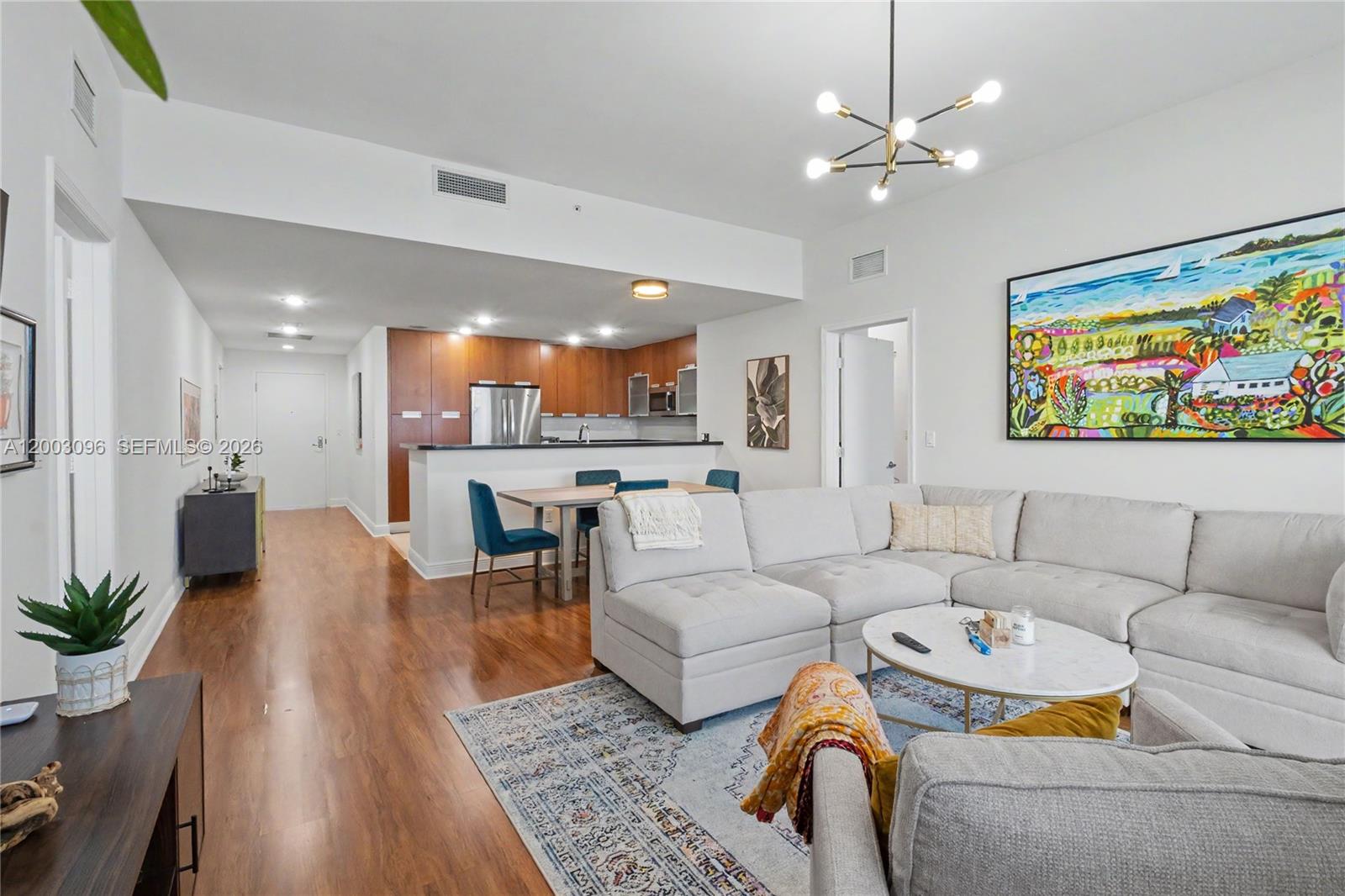 An open-concept living room and kitchen area features wood flooring, a sectional sofa, and cabinetry — 7901 Hispanola Ave # 1810, Miami FL 33141, MIAMI, FL