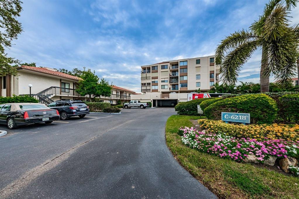 An exterior view of a multi-story apartment building with a parking lot and landscaping — 6218 PALMA DEL MAR BOULEVARD S UNIT 507, ST PETERSBURG, FL