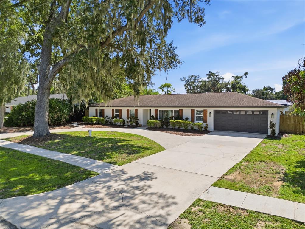 A single-story house with a white exterior, dark garage door, and a large oak tree — 706 S OAKWOOD AVENUE, BRANDON, FL