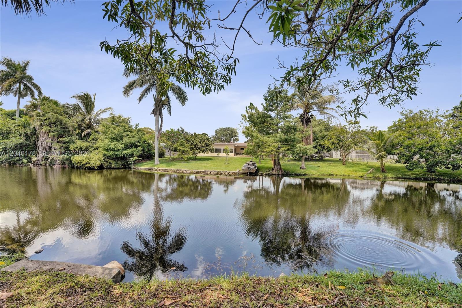 A grassy backyard with trees and a small boat overlooks a calm pond — 9120 SW 49th St, Cooper City FL 33328, COOPER CITY, FL
