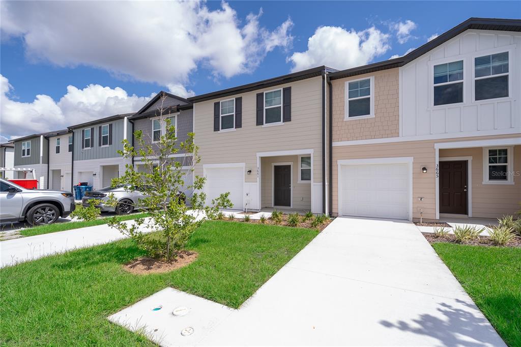 A row of modern townhomes features tan and white siding, attached garages, and concrete driveways — 3661 SPIRE DRIVE, DAVENPORT, FL