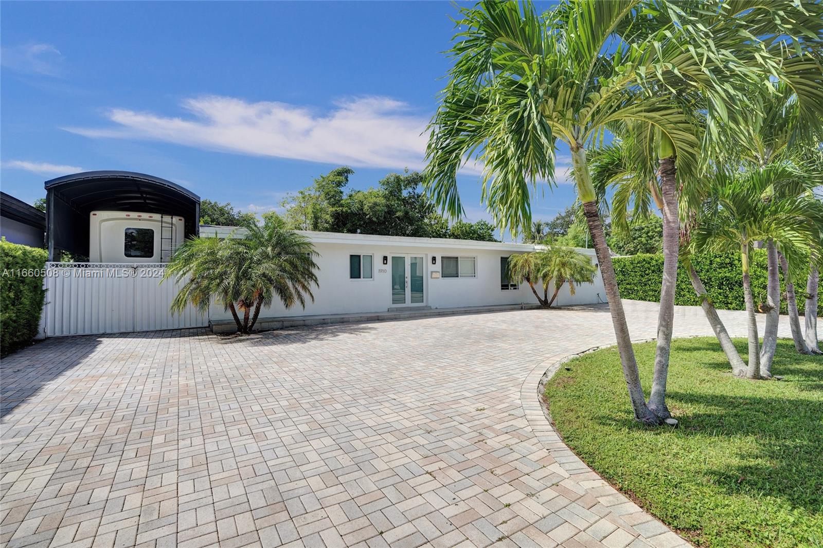 A white single-story house features a paved driveway, palm trees, and a covered RV port — 1910 N Hibiscus Dr, North Miami FL 33181, NORTH MIAMI, FL