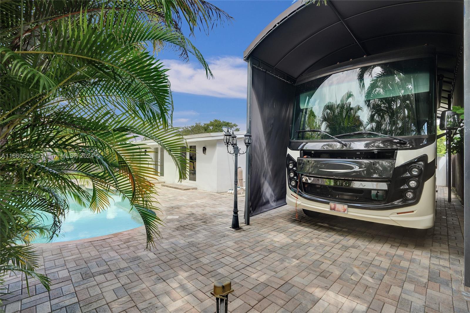 A large recreational vehicle is parked under a metal canopy beside a swimming pool — 1910 N Hibiscus Dr, North Miami FL 33181, NORTH MIAMI, FL