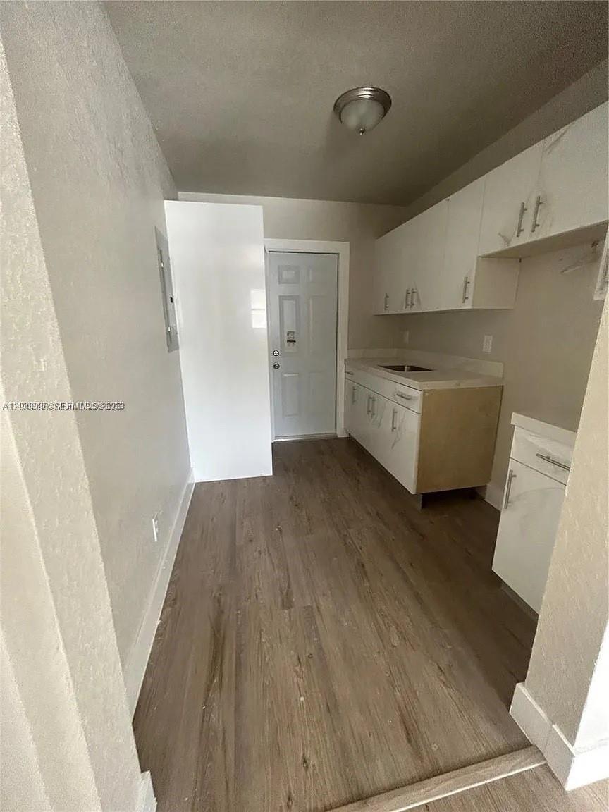 A small kitchen features white cabinets, a sink, and wood-look flooring — 10540 SW 172nd St, Miami FL 33157, MIAMI, FL