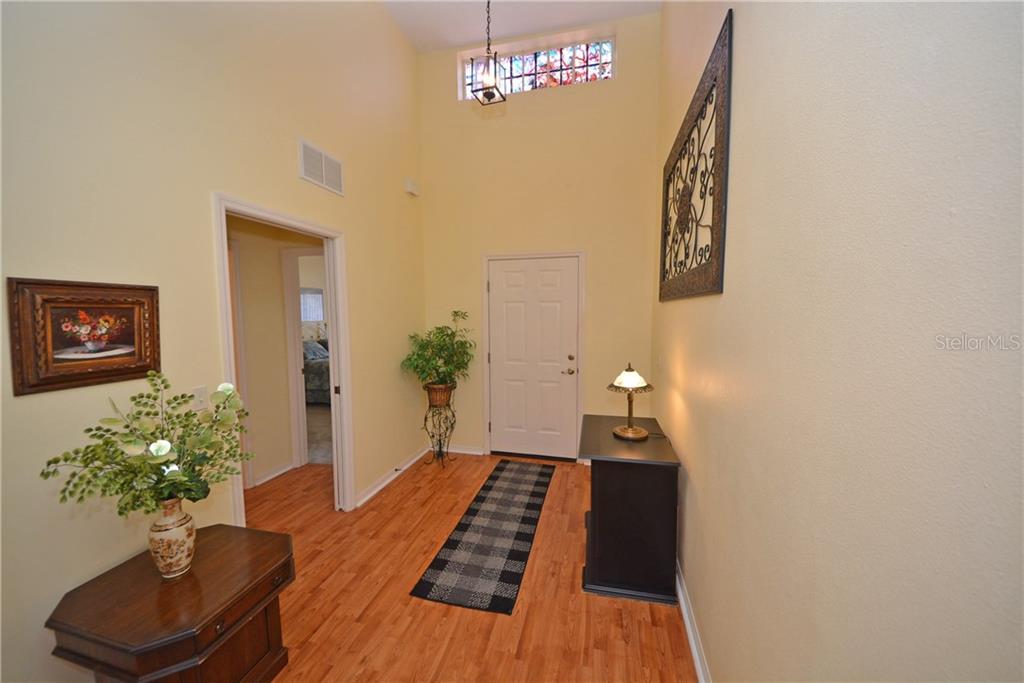 A high-ceilinged entryway features wood-look flooring, a white front door, and a black console table — 4314 BERWICK DRIVE, LAKE WALES, FL