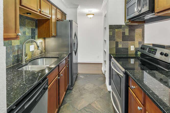 A galley kitchen features wood cabinets, dark granite countertops, stainless steel appliances, and slate flooring — 2311 N Congress Avenue # 28, Boynton Beach FL 33426, BOYNTON BEACH, FL