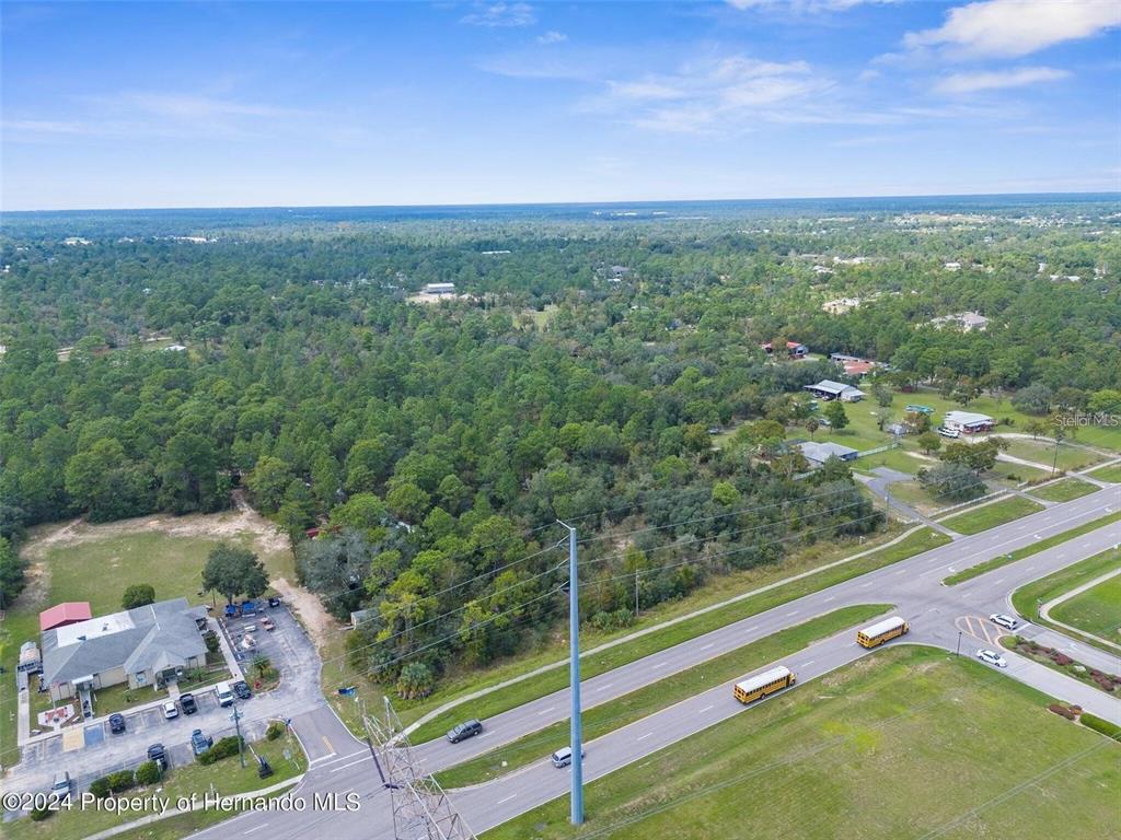 An aerial view shows a wooded lot adjacent to a road with school buses — SUNSHINE GROVE ROAD, BROOKSVILLE, FL