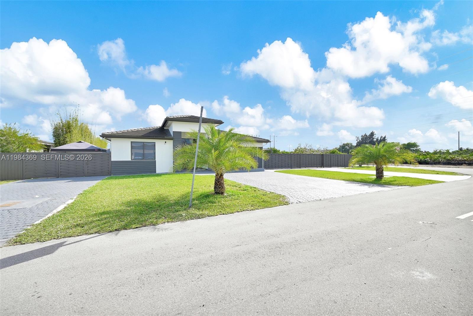 A modern single-story house features a paved driveway, two palm trees, and a dark fence — 13334 SW 227th St, Miami FL 33170, MIAMI, FL