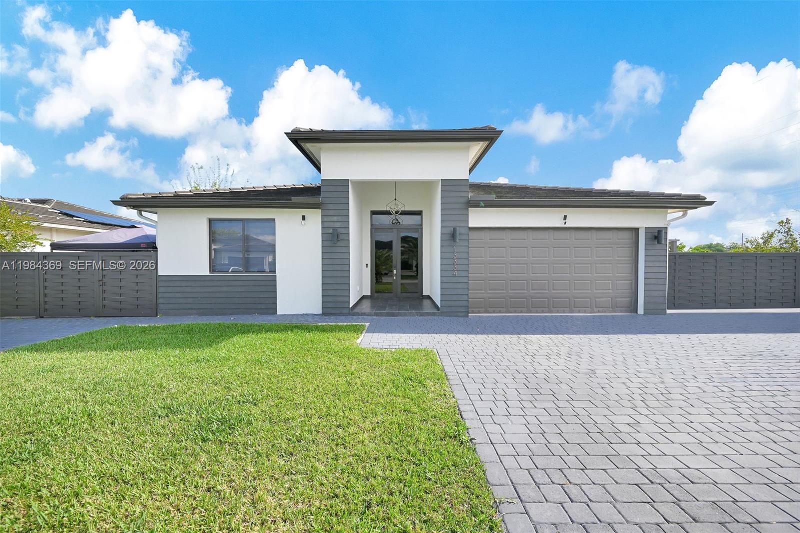 A single-story house features a gray and white exterior with a paved driveway and lawn — 13334 SW 227th St, Miami FL 33170, MIAMI, FL
