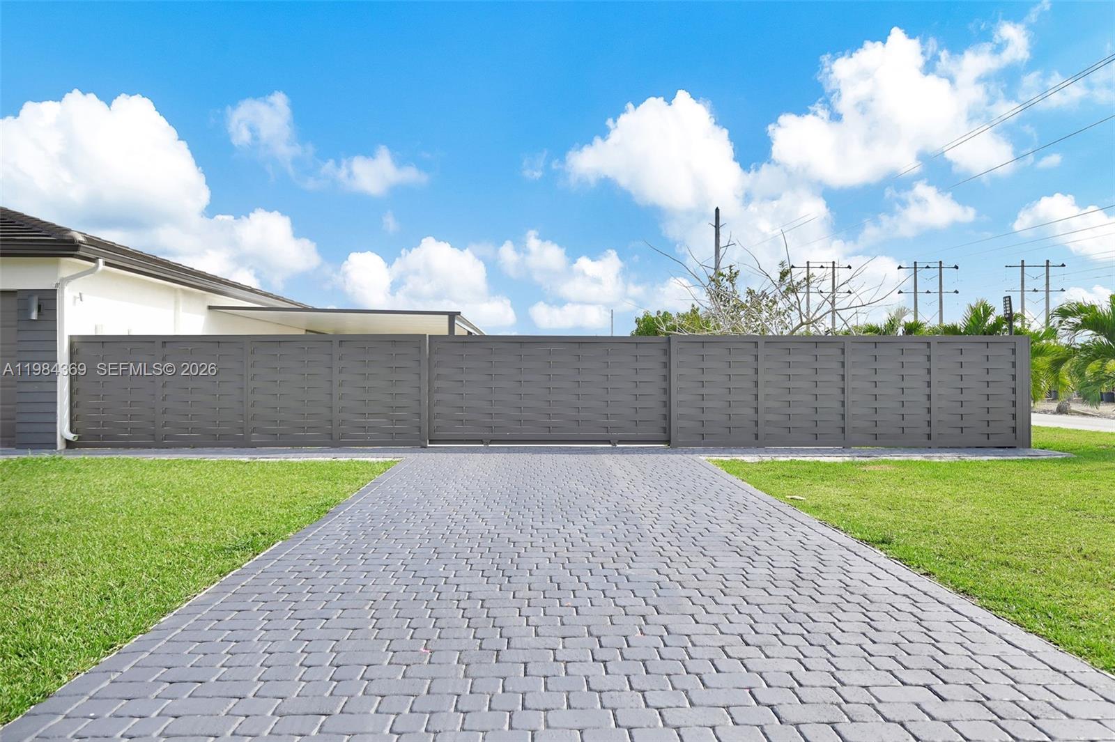 A paved driveway leads to a modern dark gray horizontal slat fence and gate — 13334 SW 227th St, Miami FL 33170, MIAMI, FL