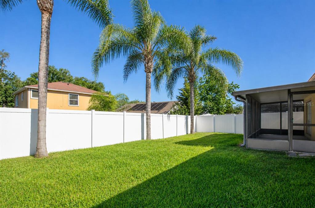 A grassy backyard features a white vinyl fence, three palm trees, and a screened patio — 1804 WESTPOINTE CIRCLE, ORLANDO, FL