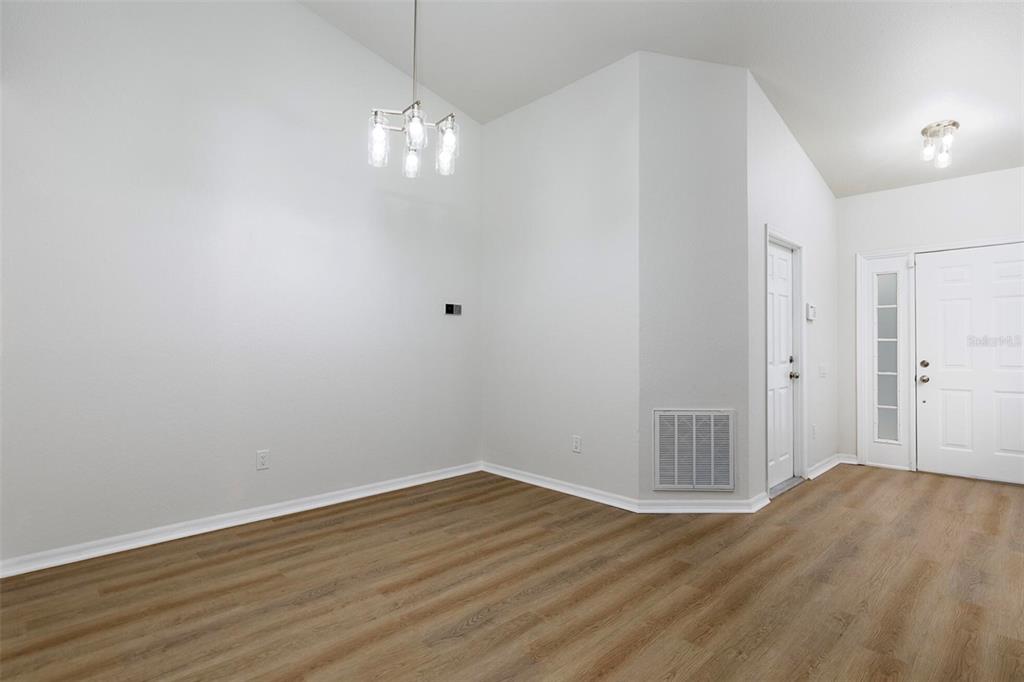 An empty room with light wood-look flooring, white walls, a chandelier, and a white door — 1804 WESTPOINTE CIRCLE, ORLANDO, FL