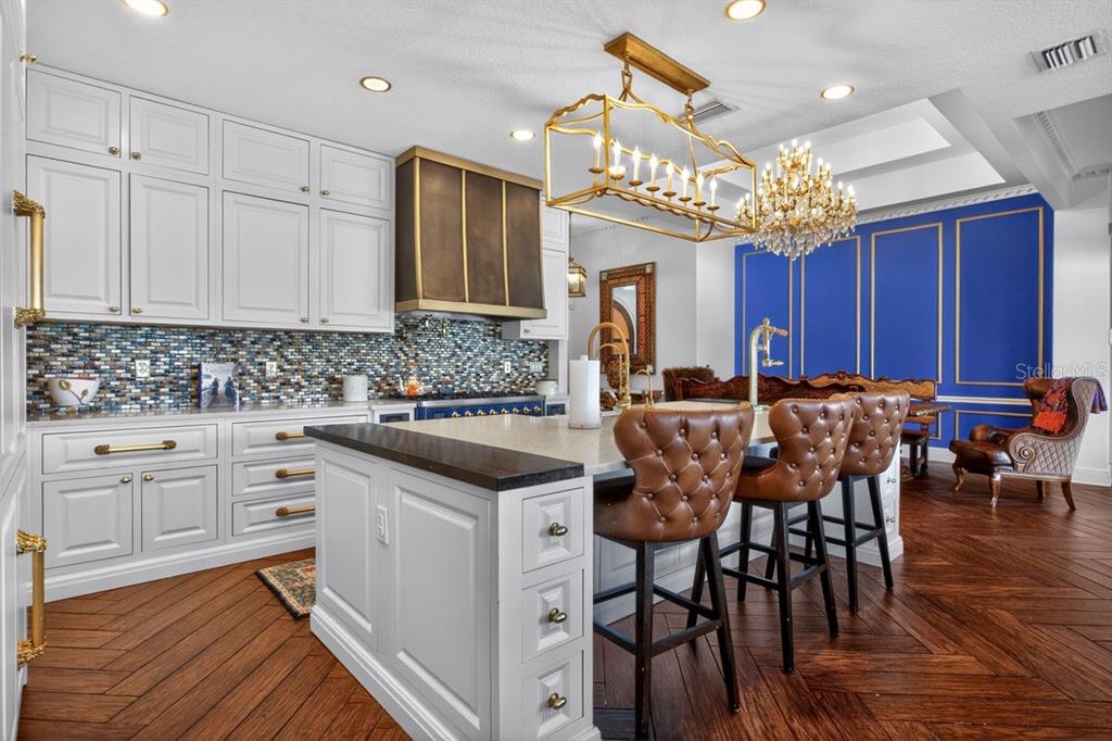 A kitchen features white cabinetry, a large island with leather stools, and a blue accent wall — 7707 HORSE FERRY ROAD, ORLANDO, FL