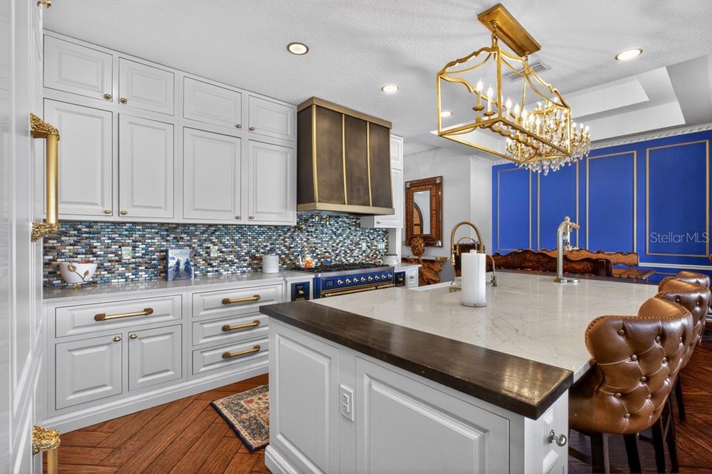 A kitchen features white cabinetry, a blue range, a large island, and a gold chandelier — 7707 HORSE FERRY ROAD, ORLANDO, FL