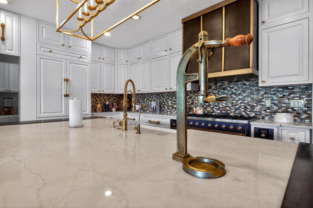 A kitchen features white cabinetry, a marble-topped island, a blue range, and a vintage press — 7707 HORSE FERRY ROAD, ORLANDO, FL