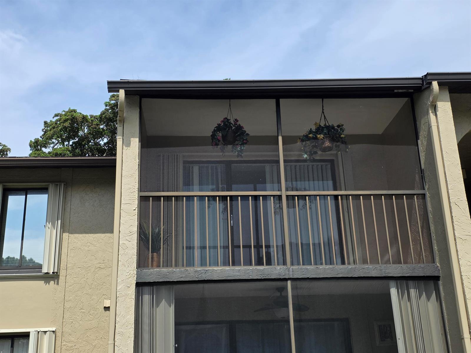 A two-story building exterior features a screened-in balcony with hanging plants and sliding doors — 715 Sunny Pine Way # A2, FL 33415, FL