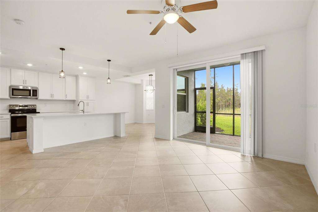 An open-concept kitchen and living area with white cabinets, tile flooring, and a sliding door — 14191 HERITAGE LANDING BOULEVARD UNIT 1216, PUNTA GORDA, FL