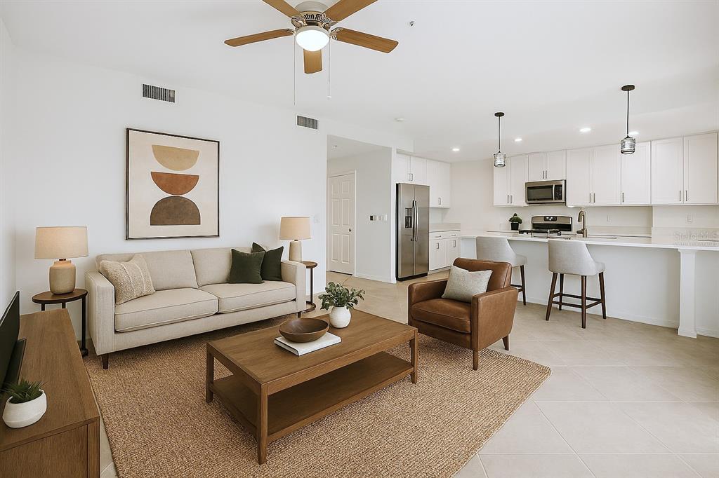 A bright open-concept living room and kitchen featuring white cabinetry, neutral furniture, and tile flooring — 14191 HERITAGE LANDING BOULEVARD UNIT 1216, PUNTA GORDA, FL